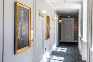 A hallway with framed portraits on the walls, wall sconces, and a patterned carpet.
