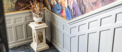 A room with a patterned carpet, a white wall with paneling, and a large mural on the wall.