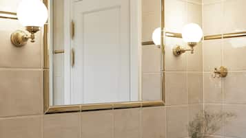 Een badkamer met een grote spiegel, twee wandlampen, een zwart wastafelmeubel en een vaas met gedroogde bloemen.