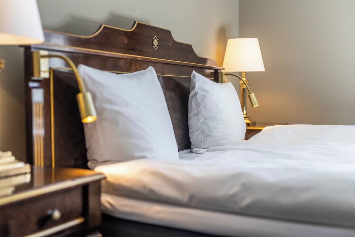 A neatly made bed with white linens, a wooden headboard, and two bedside lamps.