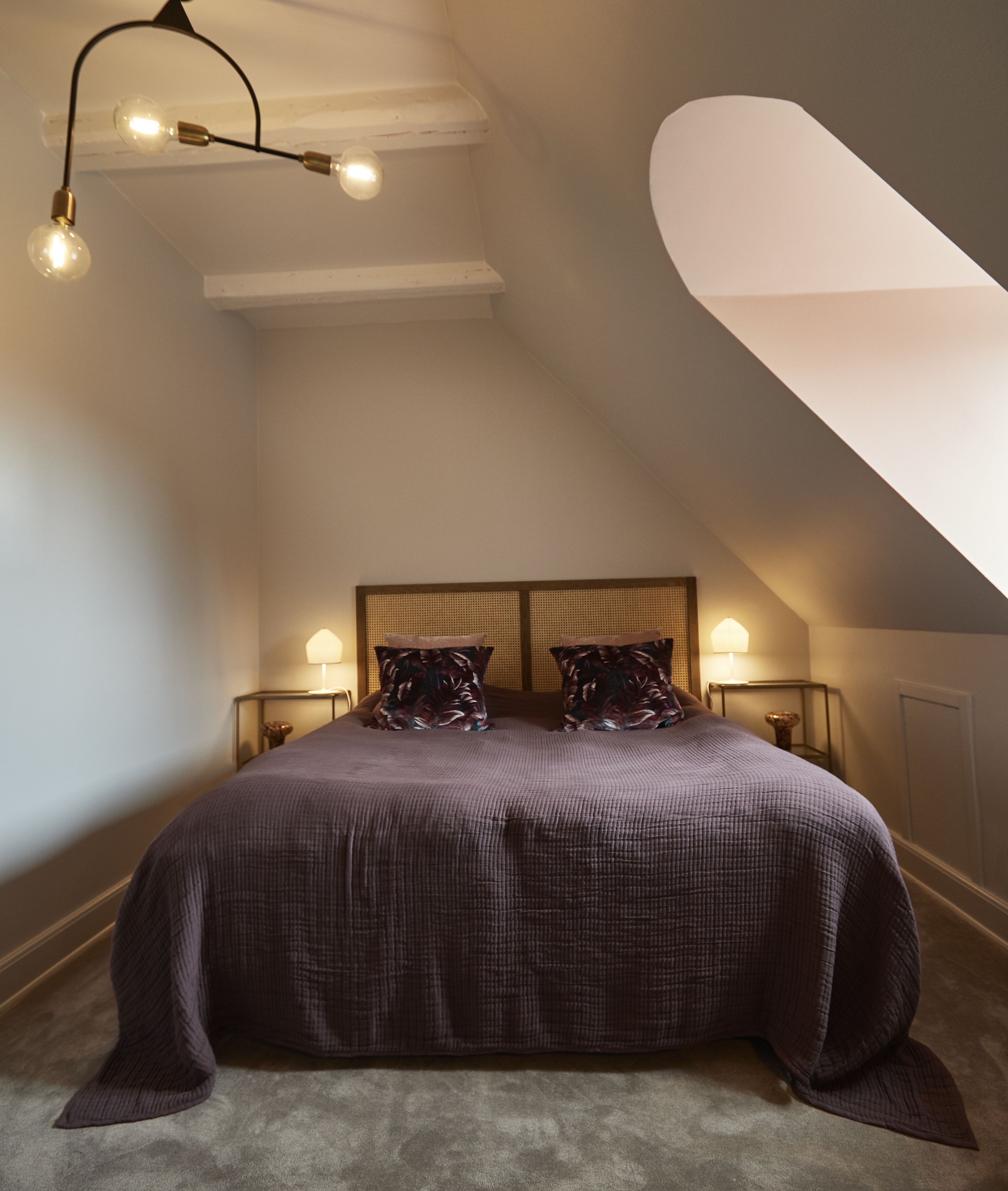 A bedroom with a large bed, a sloped ceiling, and a skylight.