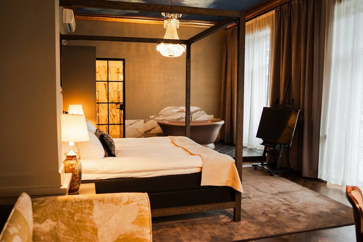 A hotel room with a bed, a desk, a chair, a bathtub, and a painting on the wall.