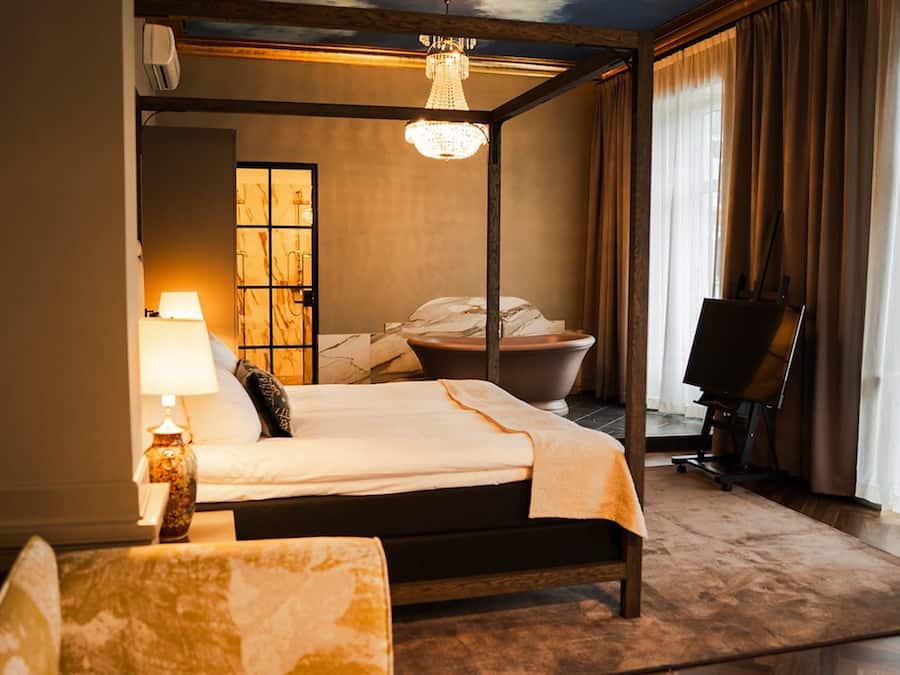 A hotel room with a bed, a desk, a chair, a bathtub, and a painting on the wall.