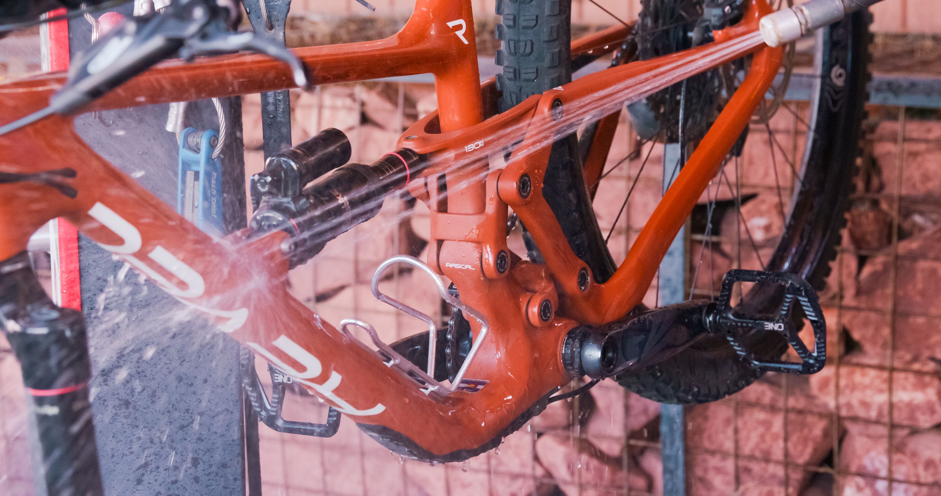 Una bicicleta con estructura roja y componentes negros, que incluye un portabebidas y pedales, sobre un soporte.