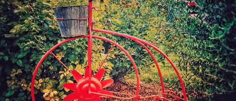 A red metal sculpture in a garden with a building in the background.