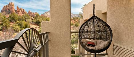 A balcony with a hanging chair overlooking a mountainous landscape.