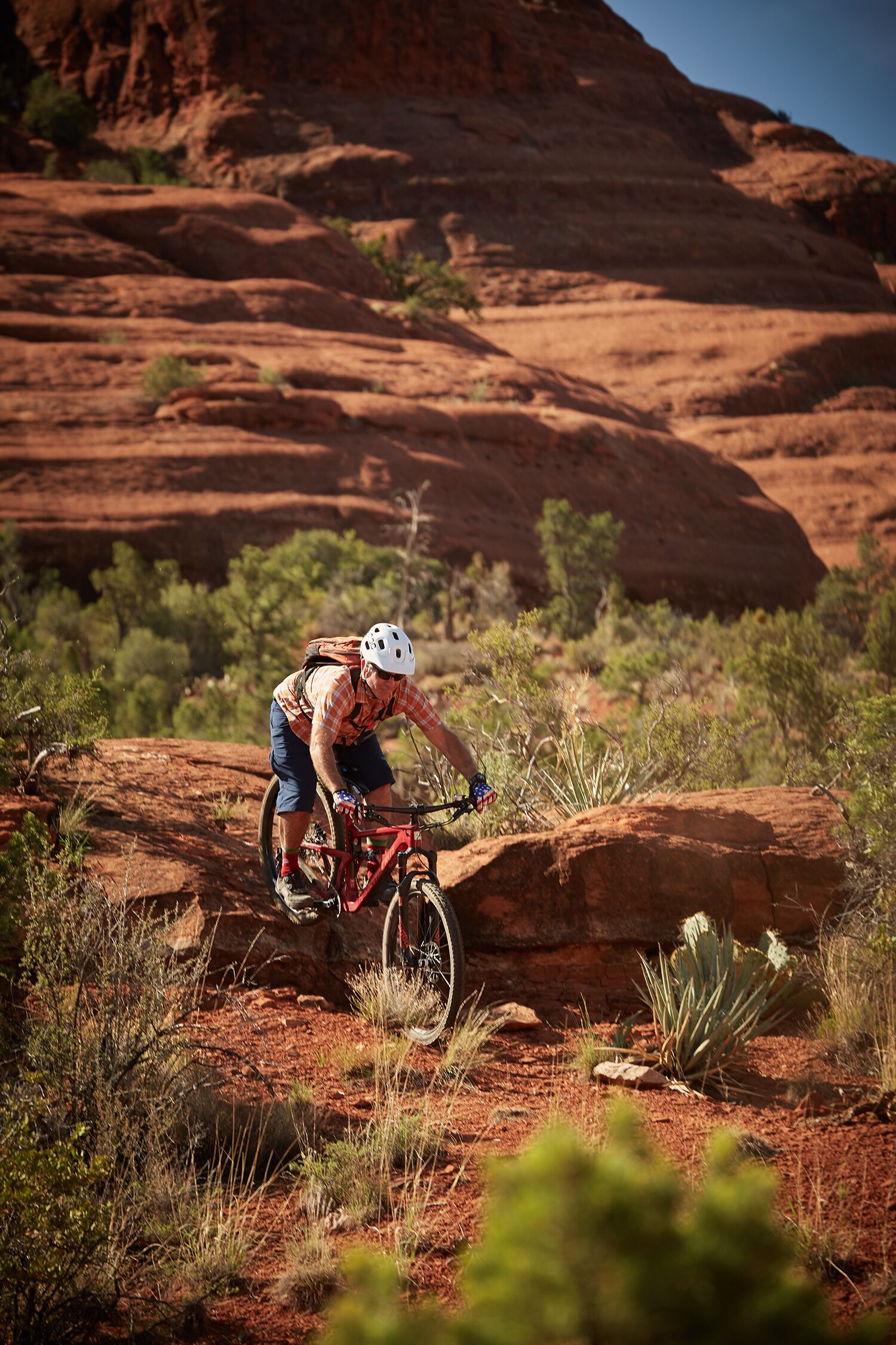 A person riding a mountain bike on a rocky terrain with sparse vegetation and a large rock formation in the background.