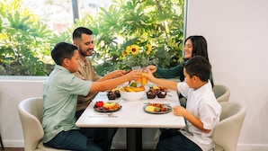 A family of four seated around a dining table with various dishes, in a room with a large window and indoor plants. - Arabella Hotel Sedona (Sedona)