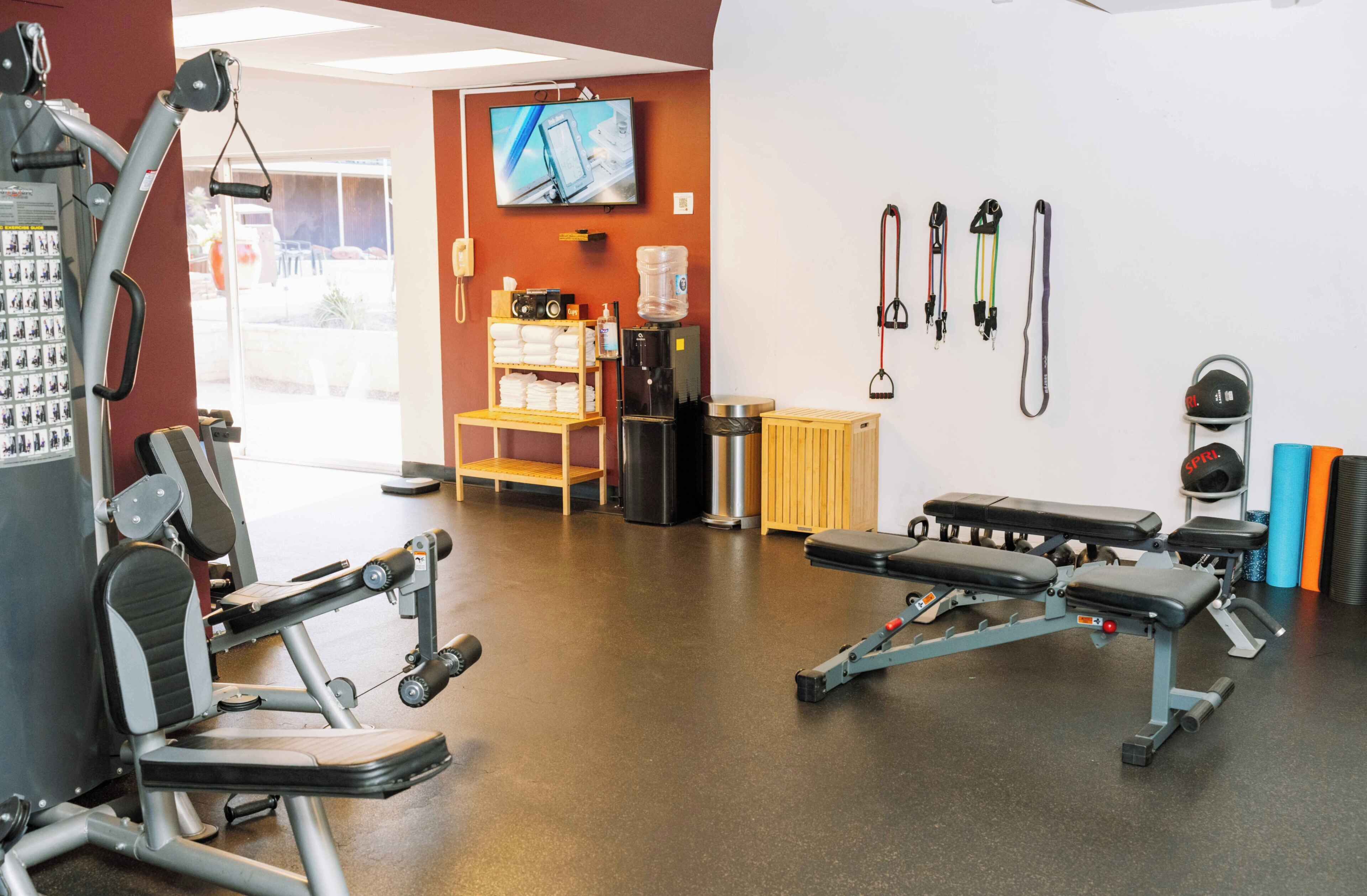 Ein Fitnessraum mit Trainingsgeräten, einem Fernseher und einem Wasserspender.