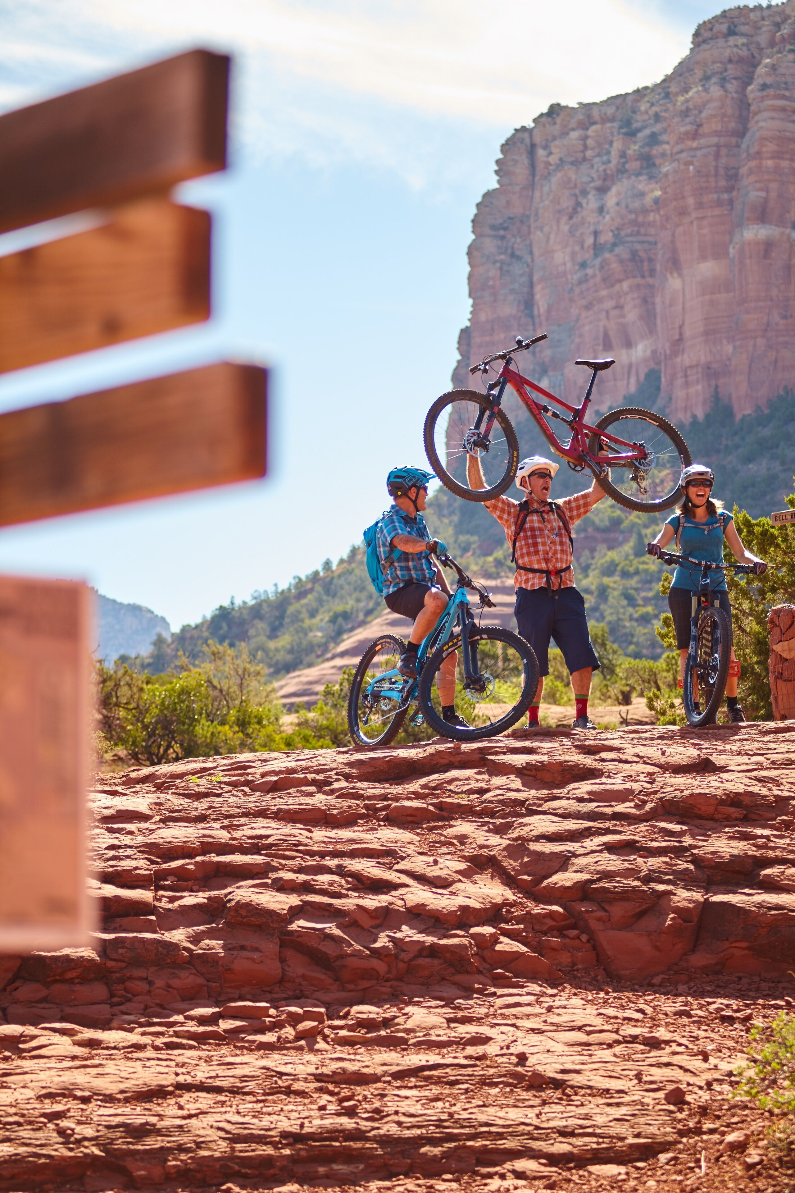 A group of people on a mountain biking trail with rocky terrain and a large rock formation in the background.