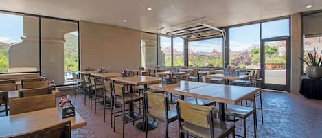Un espace de restauration intérieur avec des tables et des chaises, de grandes fenêtres et une vue sur un paysage montagneux.