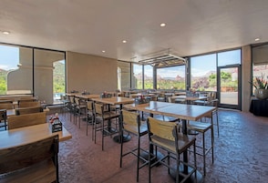 Un comedor interior con mesas y sillas, ventanas amplias y vistas a un paisaje montañoso.