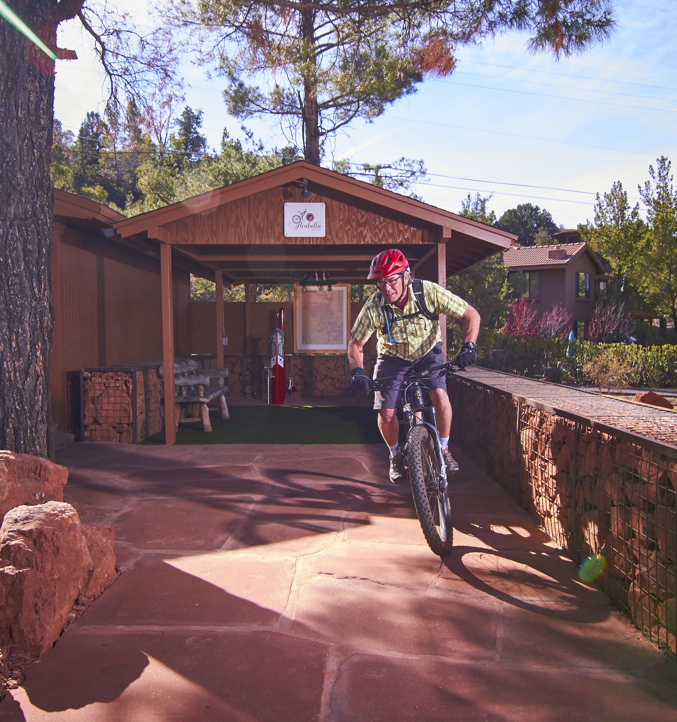 A man riding a bicycle on a paved path in front of a wooden building with a sign that reads "Arabella."