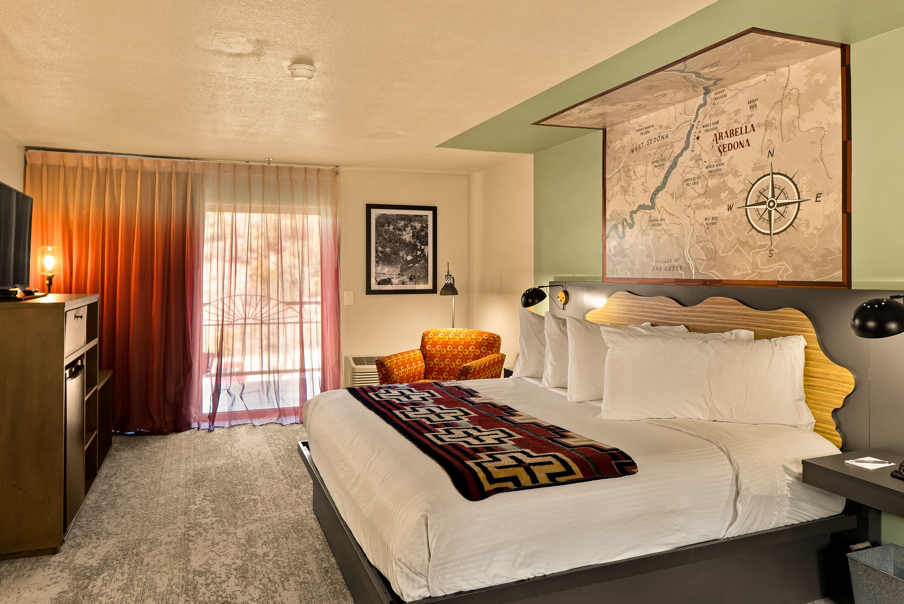 A hotel room with a large bed, a map on the wall, a desk, and a chair.