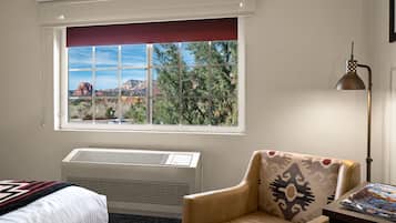 Ein Hotelzimmer mit großem Fenster, einem Bett, einem Sessel, einem Tisch und einer Lampe.