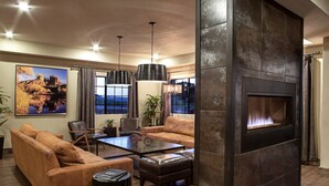 A modern living room with a fireplace, leather sofas, a coffee table, and a large window with curtains. - Arabella Hotel Sedona (Sedona)