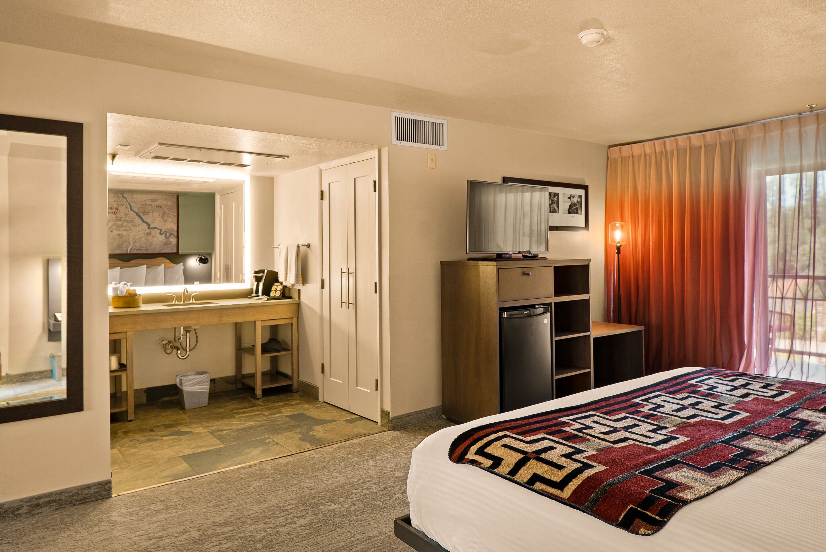 A hotel room with a bed, a television, a desk with a sink, and a wardrobe.
