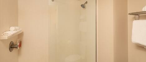 A glass-enclosed shower stall with a towel rack and a toilet visible in the adjacent room.