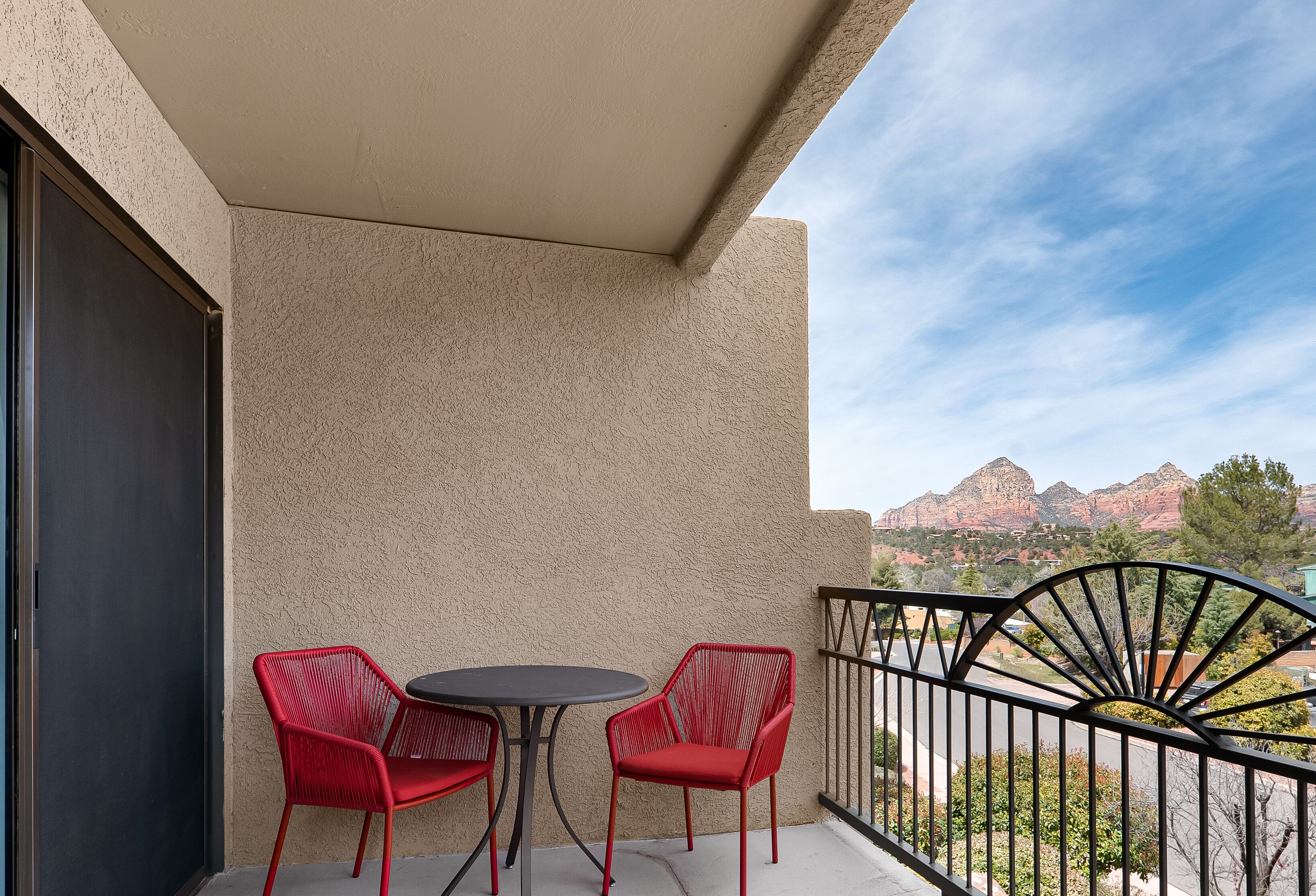 A balcony with two red chairs and a small round table, overlooking a mountain range.