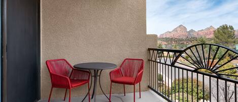 A balcony with two red chairs and a small round table, overlooking a mountain range.