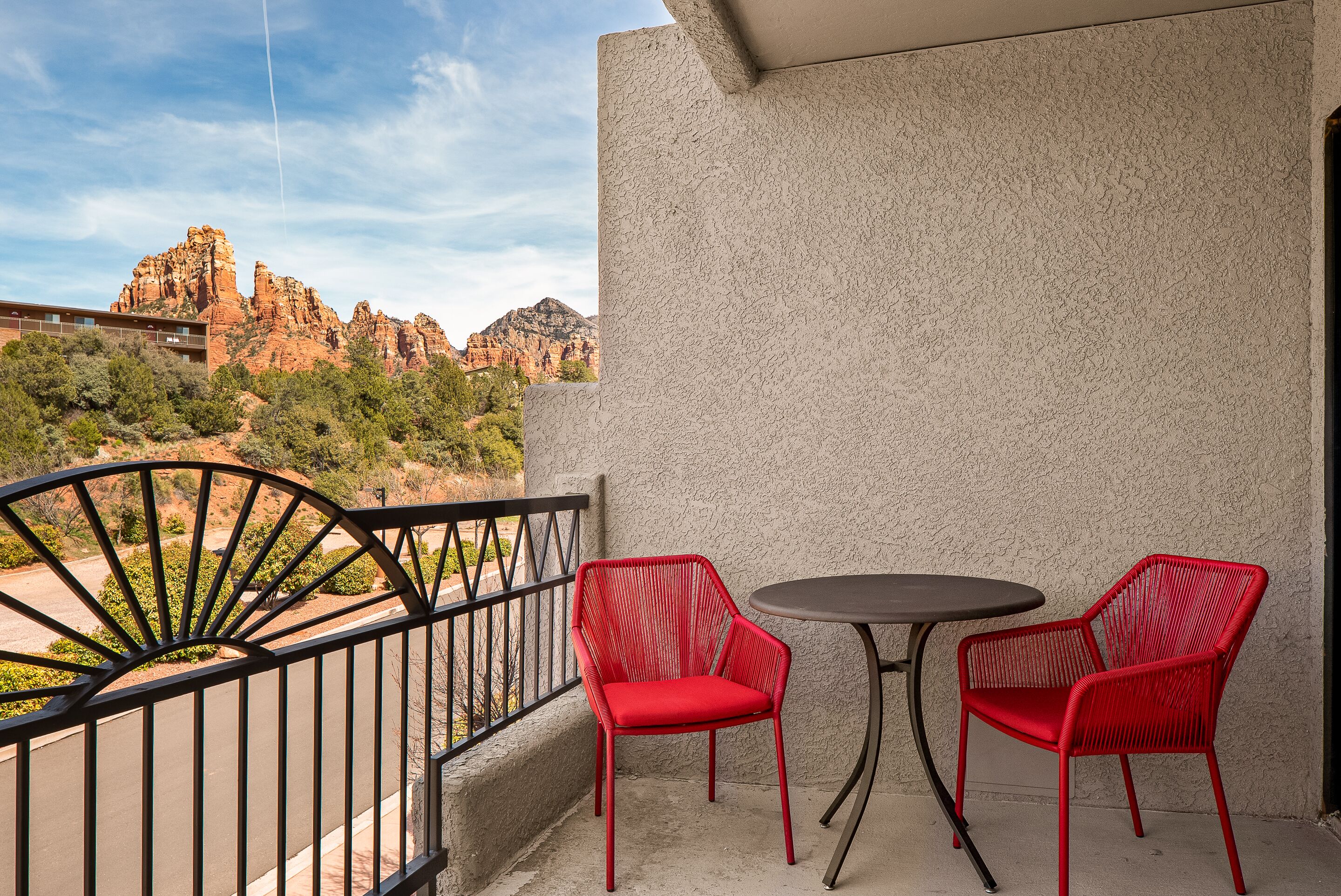 A balcony with two red chairs and a small round table, overlooking a mountainous landscape.