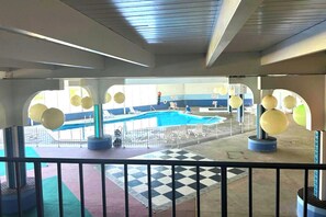 Zona de piscina con suelo a cuadros, sillas de descanso y vistas a la piscina a través de una barrera de vidrio.