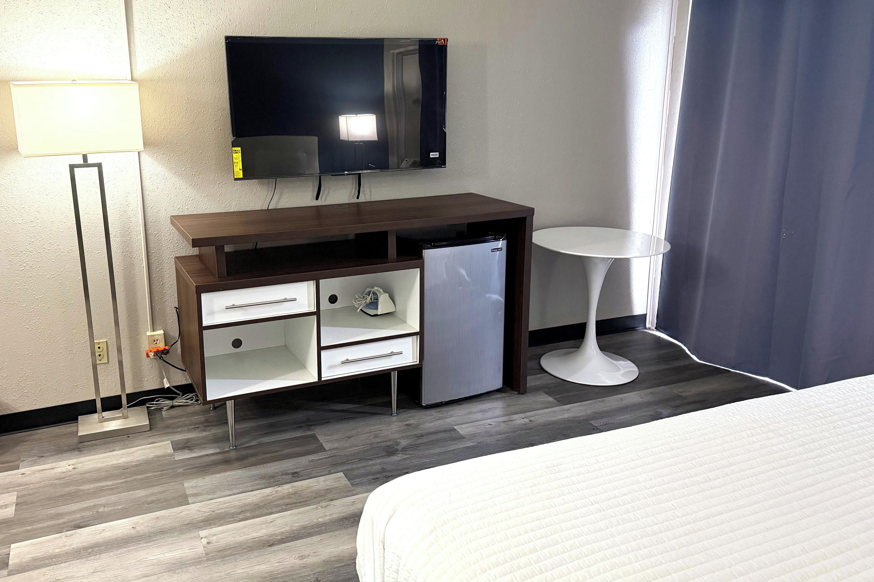 Una habitación de hotel con una cama, un escritorio con refrigerador, un televisor y una mesita.