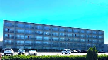 Un edificio de varios pisos con fachada plana, varios balcones y un estacionamiento con diferentes automóviles.