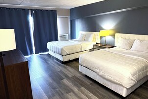 Habitación de hotel con dos camas, un escritorio, una lámpara y una ventana con cortinas.
