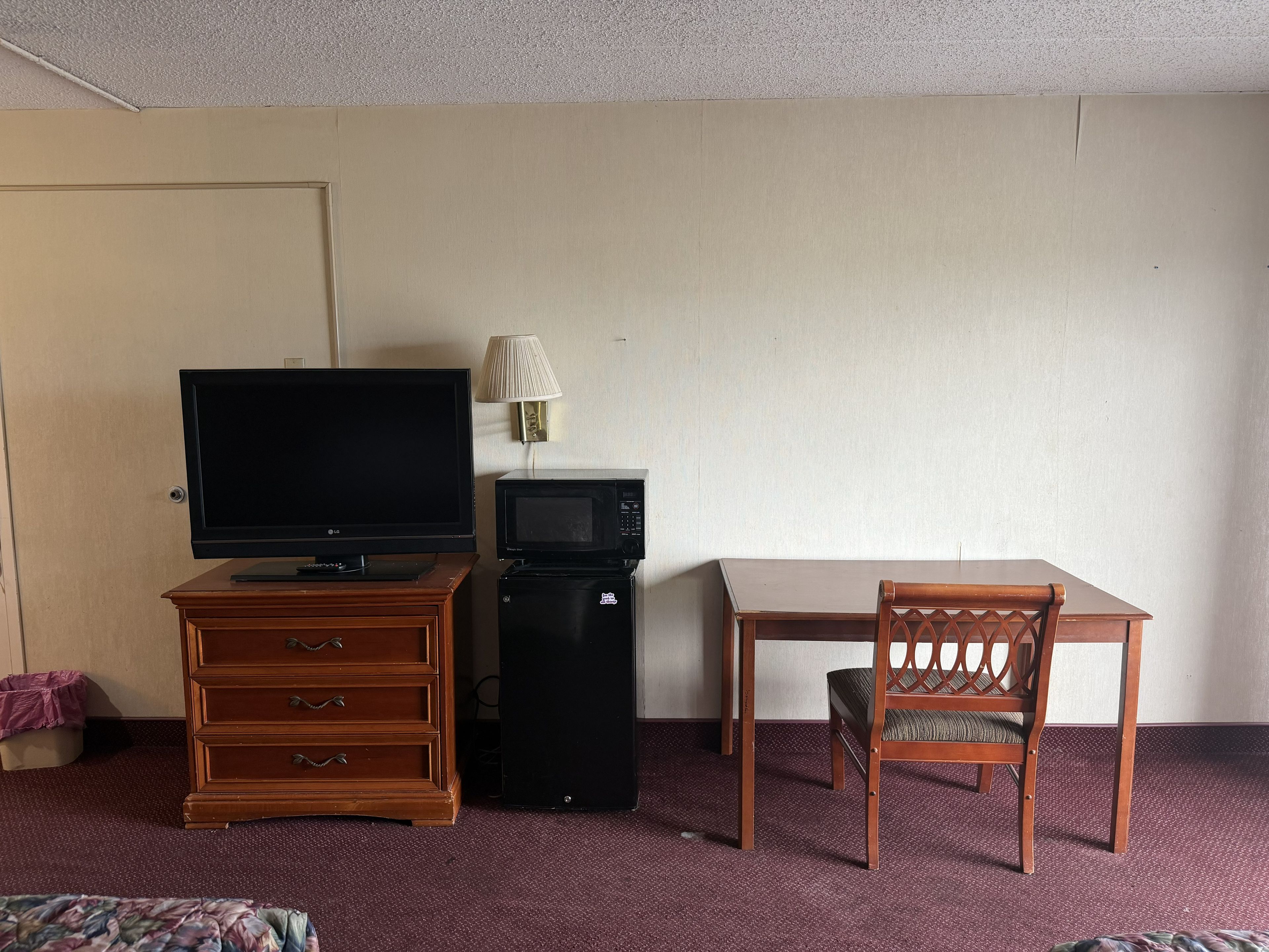 Ein Hotelzimmer mit Fernseher, Mikrowelle, einem Holzkleiderschrank, einem Esstisch und einem Stuhl.
