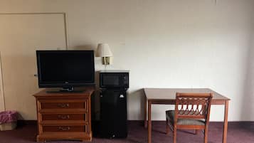 Una habitación de hotel con televisión, microondas, cómoda de madera, mesa de comedor y una silla.