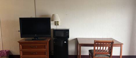 A hotel room with a television, a microwave, a wooden dresser, a dining table, and a chair.
