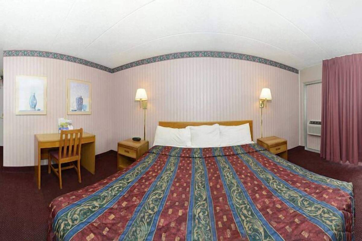 Habitación de hotel con cama, escritorio, silla, dos lámparas de noche y vistas al exterior.