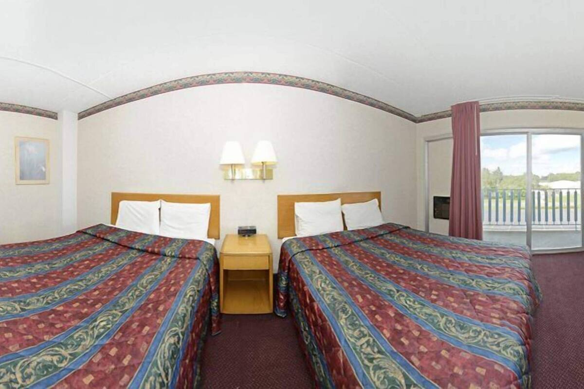 Habitación de hotel con dos camas, una mesita pequeña, dos lámparas de pared y un balcón con vistas.