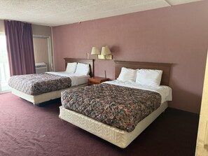 A hotel room with two beds, a window with curtains, a wall-mounted lamp, and a carpeted floor. - Twin City Inn & Suites Benton Harbor - St. Joseph (Benton Harbor)
