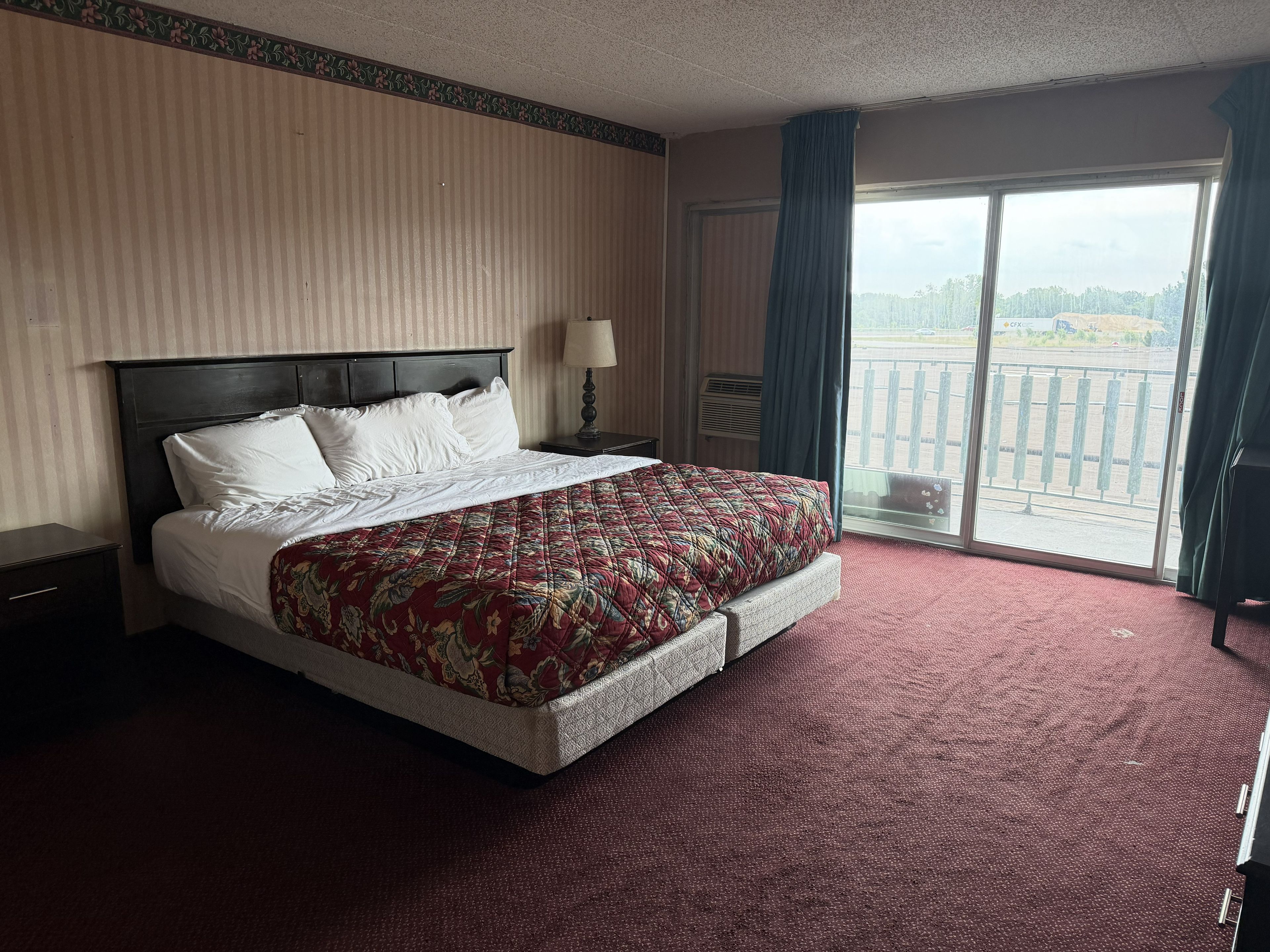 Una habitación de hotel con una cama grande, una mesita de noche, una ventana con cortinas y vistas a un paisaje lejano.