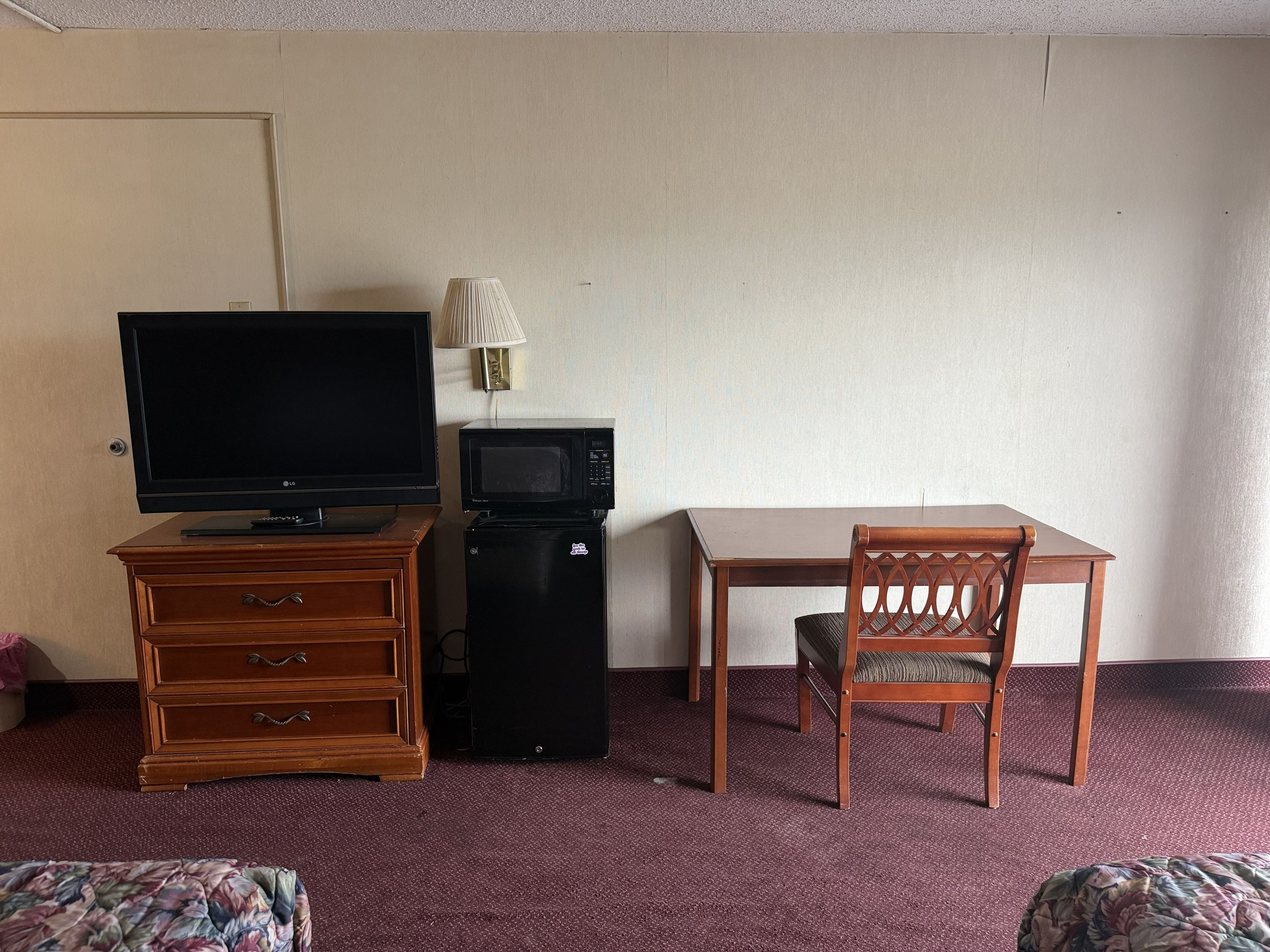 Ein Hotelzimmer mit Fernseher, Mikrowelle, kleinem Kühlschrank, Schreibtisch aus Holz und einem Sessel.