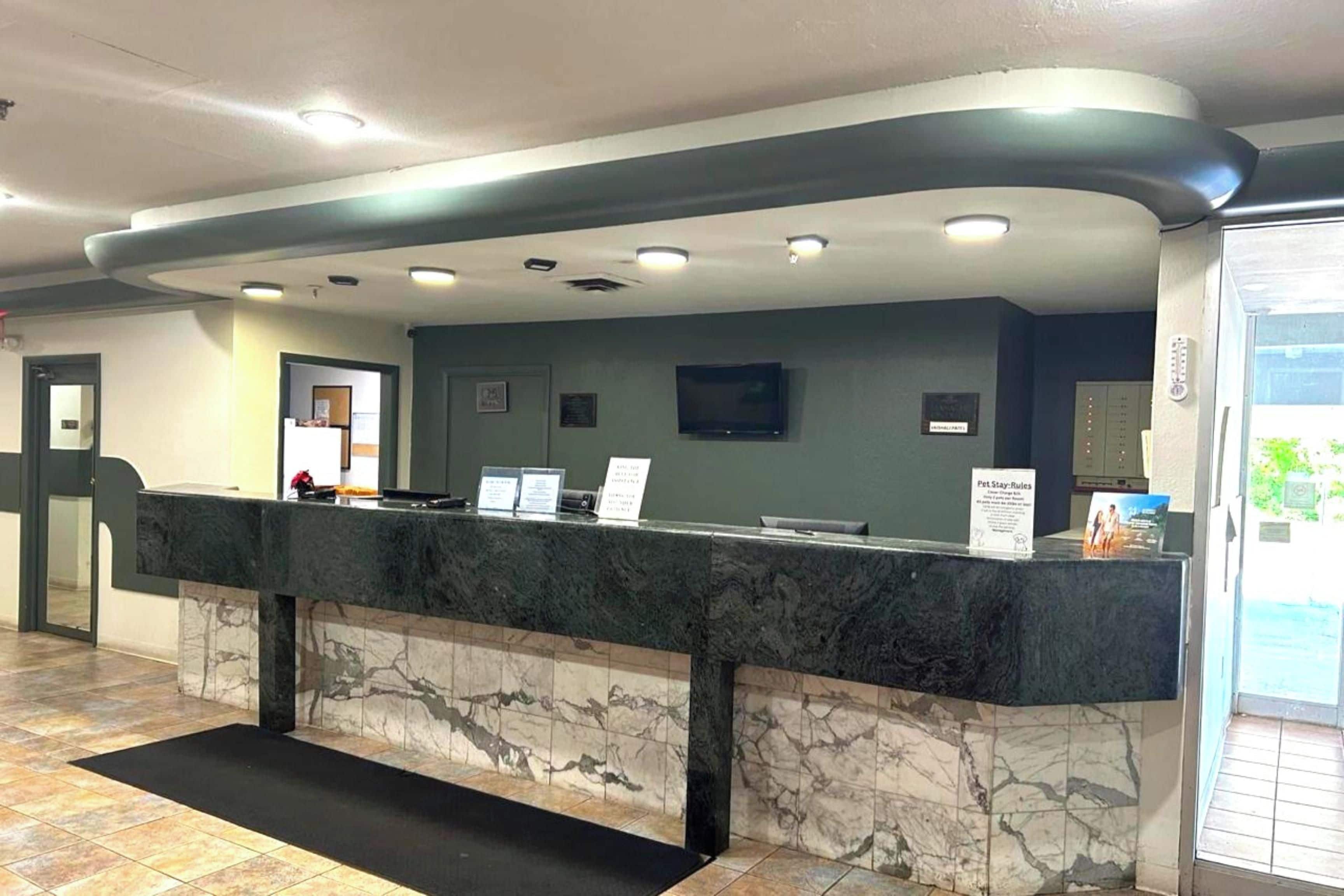 A reception desk with a marble counter, a flat-screen TV above it, and a sign with pet stay rules.
