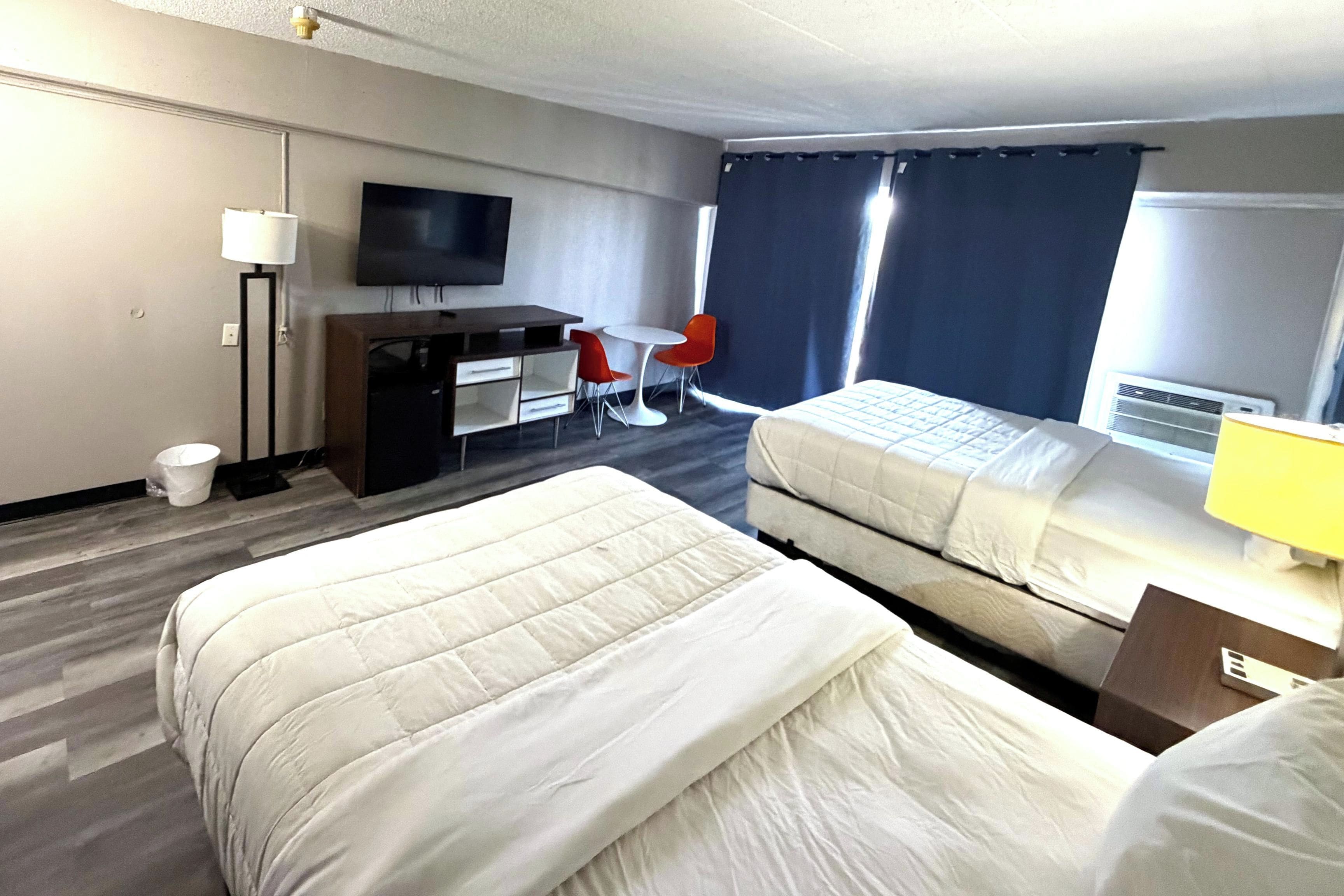 A hotel room with two beds, a desk, a chair, a TV, and a window with curtains.