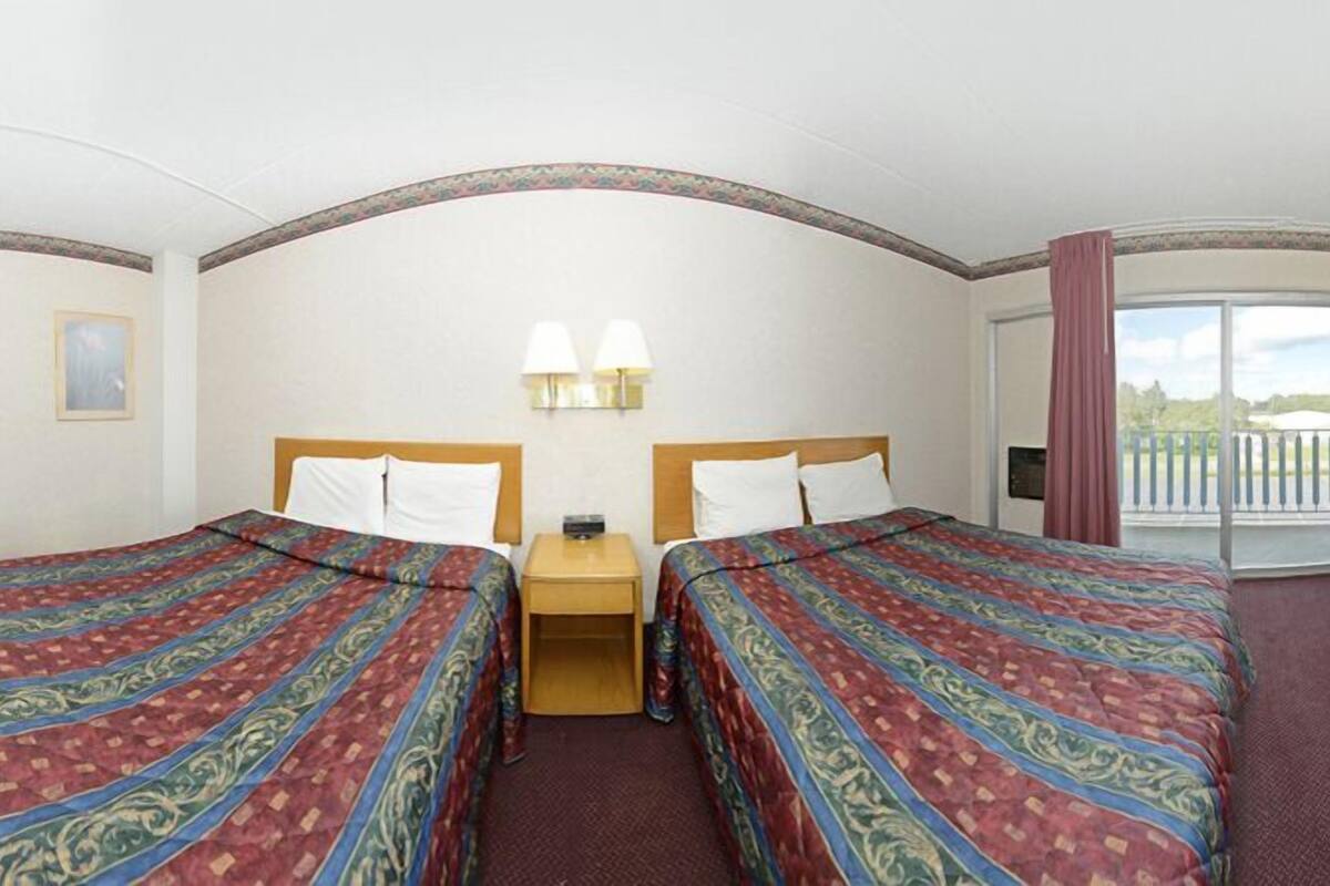 Habitación de hotel con dos camas, una mesita, dos lámparas de pared y un balcón con barandilla.