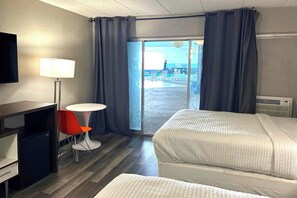 Habitación de hotel con dos camas, un escritorio, una silla, una lámpara y vista al área de la piscina.