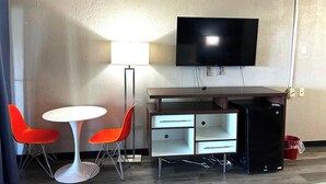 Una habitación pequeña y amoblada con escritorio, dos sillas, televisor y refrigerador.