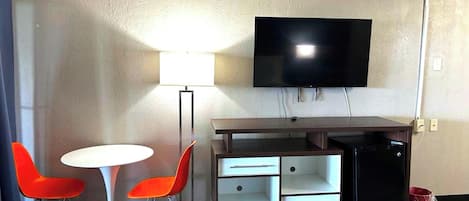 Una habitación pequeña y amoblada con escritorio, dos sillas, televisor y refrigerador.