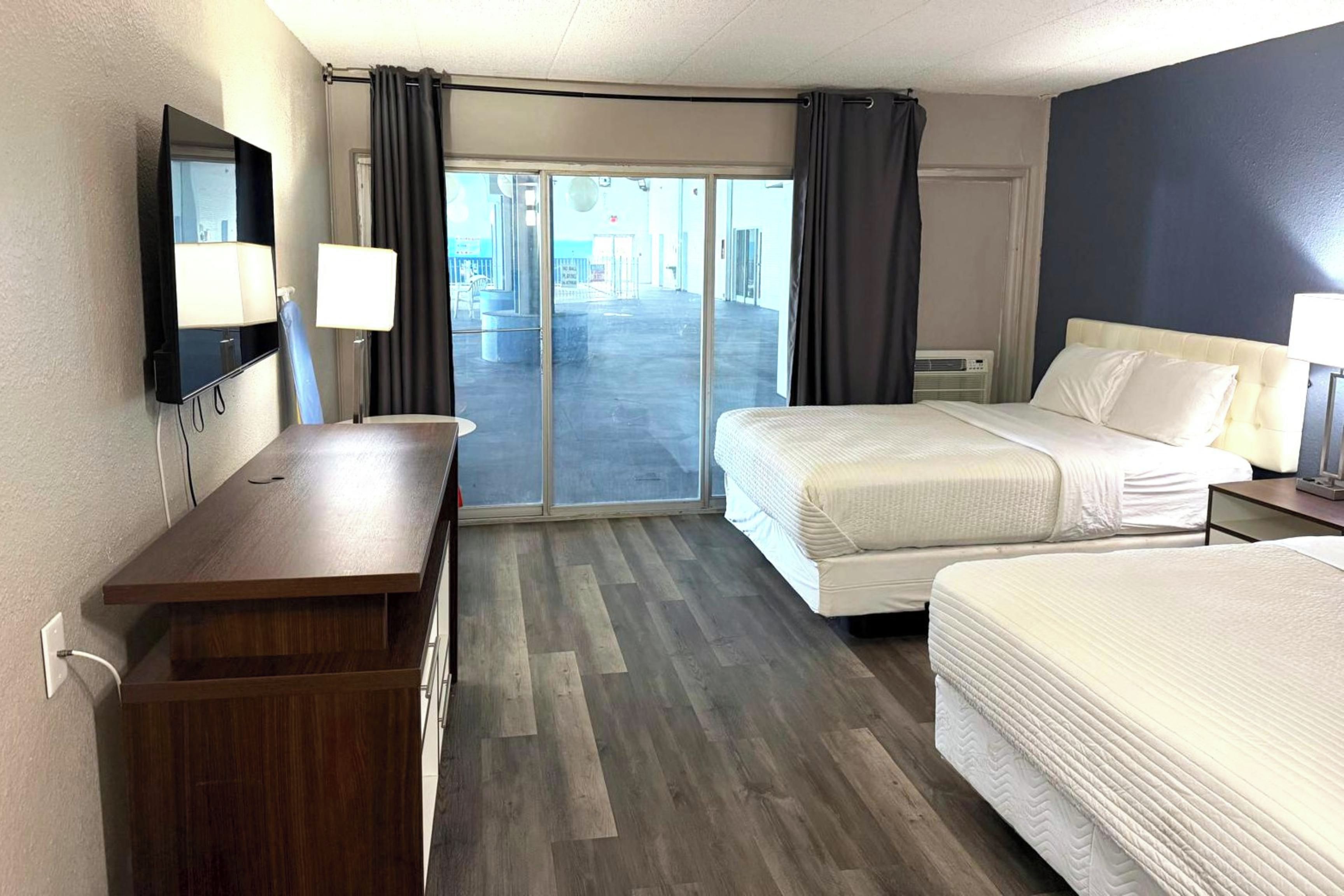 A hotel room with a bed, a desk, a TV, and a view of the outside.