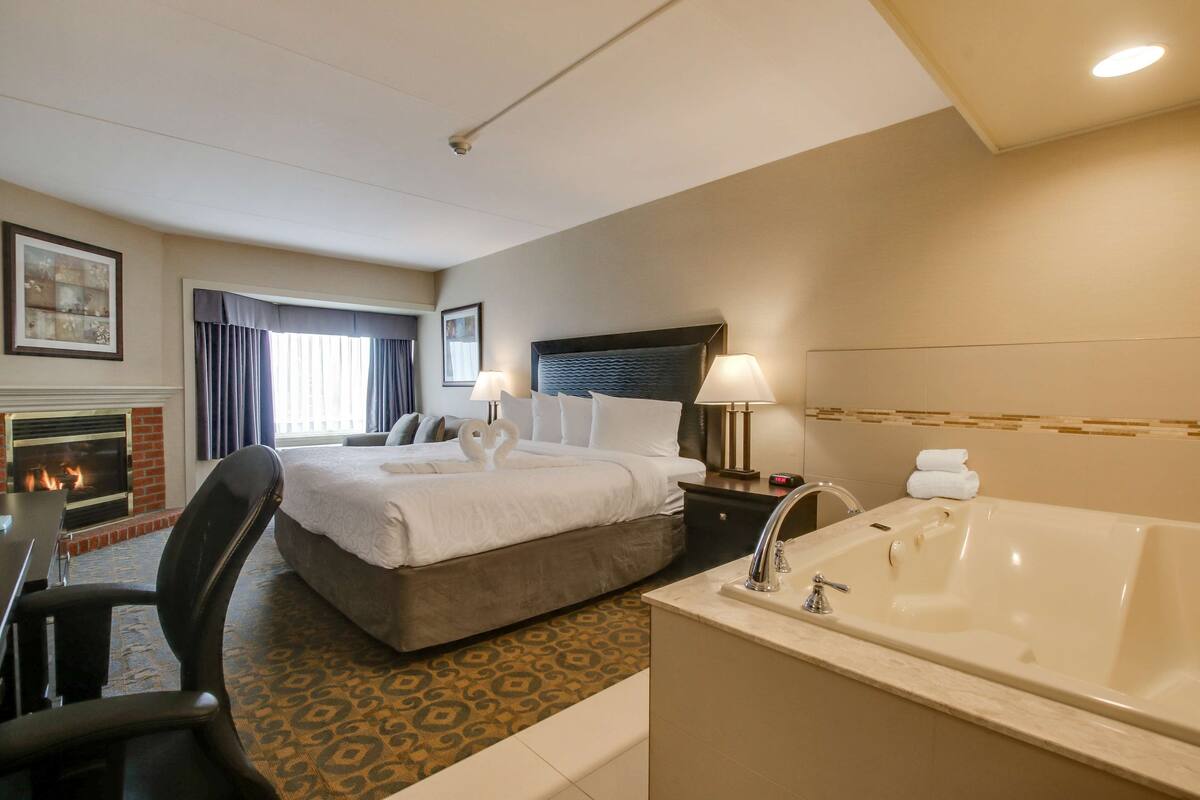 Habitación de hotel con una cama grande, una zona de estar con una silla, chimenea, una bañera grande y un escritorio.