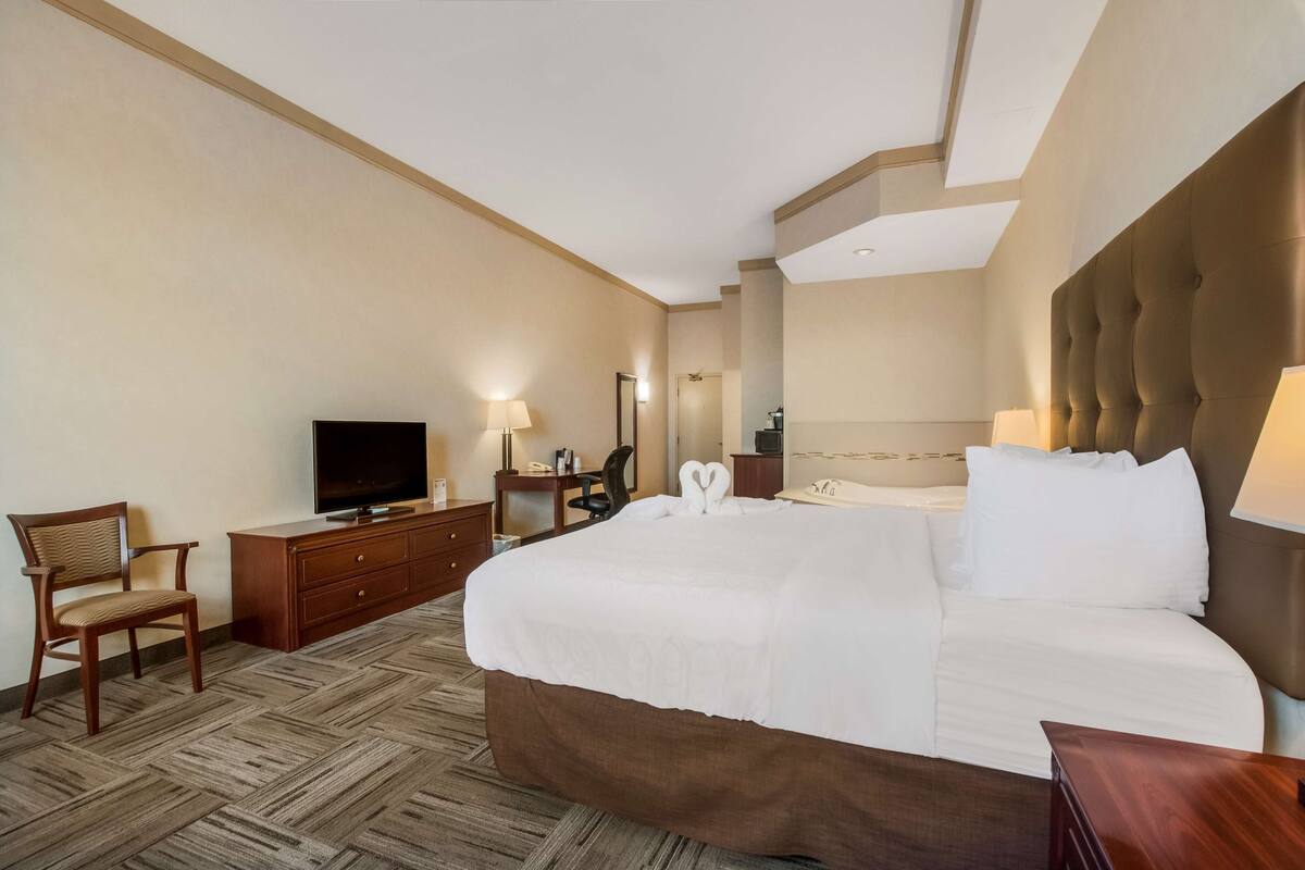 Una habitación de hotel con una cama grande, un televisor sobre una cómoda de madera, una silla y un escritorio con una lámpara.