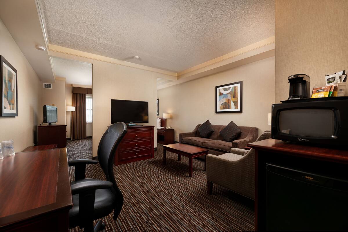 Habitación de hotel con un escritorio de madera, televisión, sofá y cafetera.
