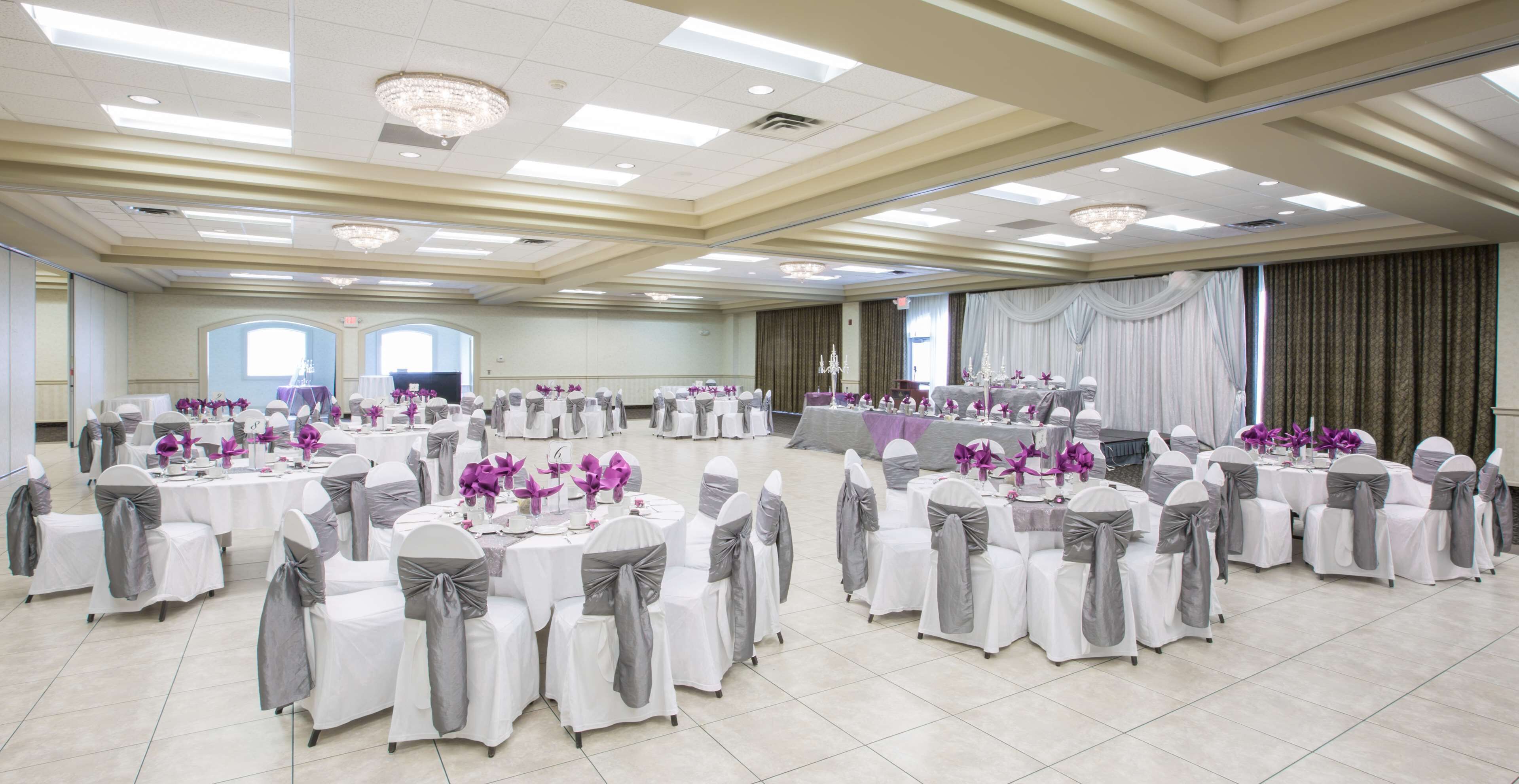 A banquet hall with round tables, chairs with grey sashes, and purple floral centerpieces.