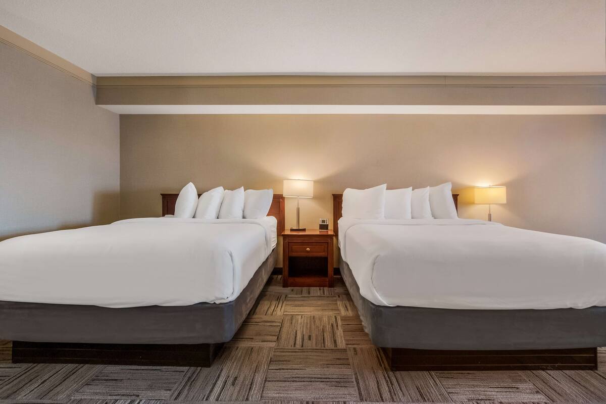 Habitación de hotel con dos camas, una mesita de noche de madera con lámparas y una alfombra estampada.