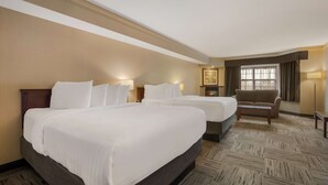 A hotel room with two beds, a sofa, a small table, and a window with curtains.